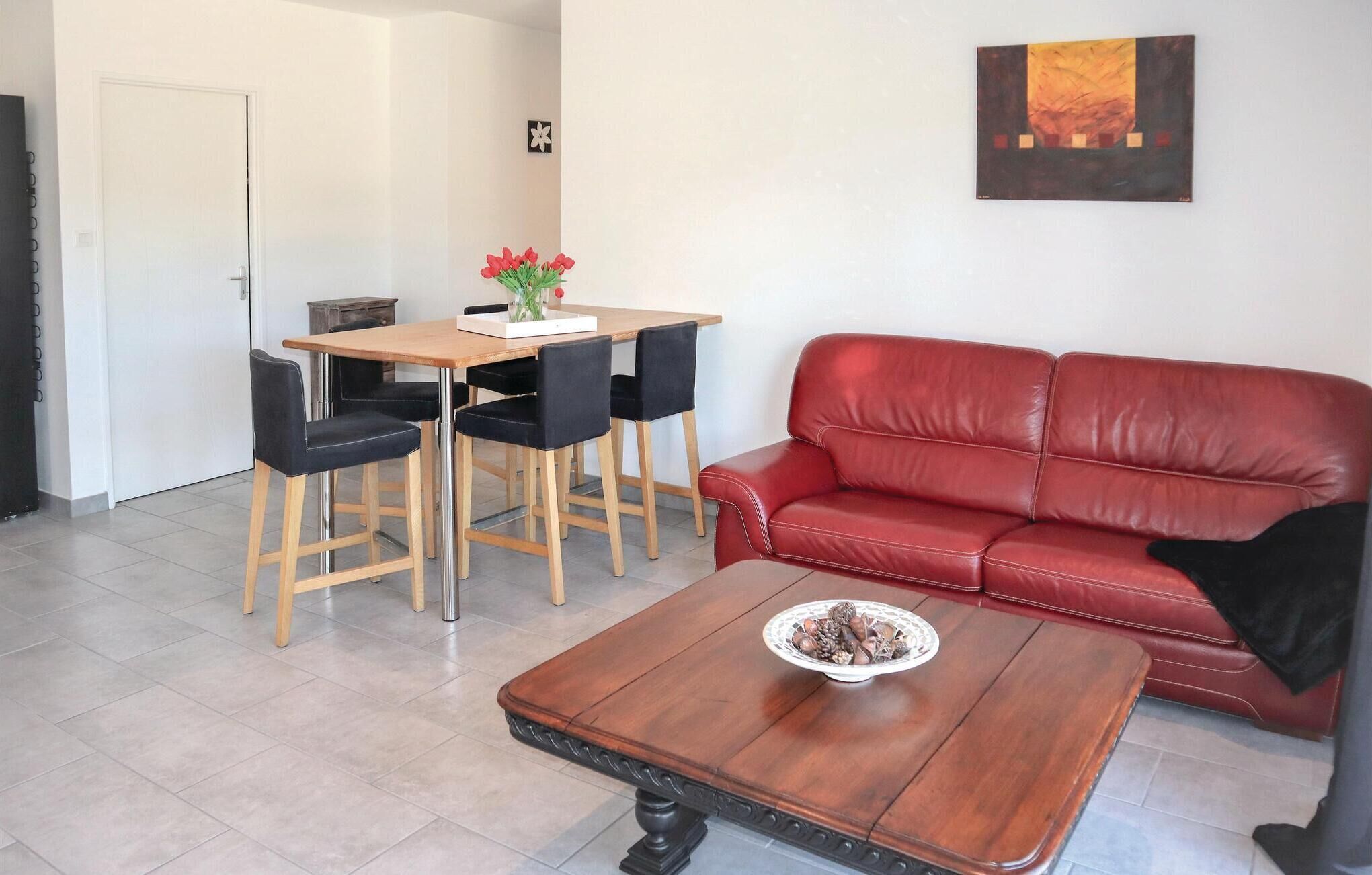A living room with a red leather sofa, a wooden coffee table with a bowl of nuts, and a dining area with a wooden table and black chairs.