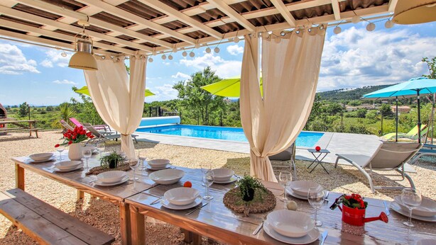 Ein Außenbereich zum Essen mit Blick auf einen Pool, überdacht mit einer Pergola und mit Tischen und Stühlen ausgestattet.