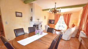 A dining area with a round wooden table, six chairs, a vase with flowers, a fireplace, a television, and a sofa.