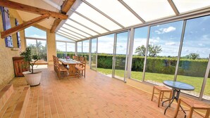 A conservatory with a brick floor, wooden furniture, and large glass doors offering a view of a garden.