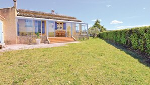 A house with a glass facade, a patio with outdoor furniture, and a well-maintained lawn.