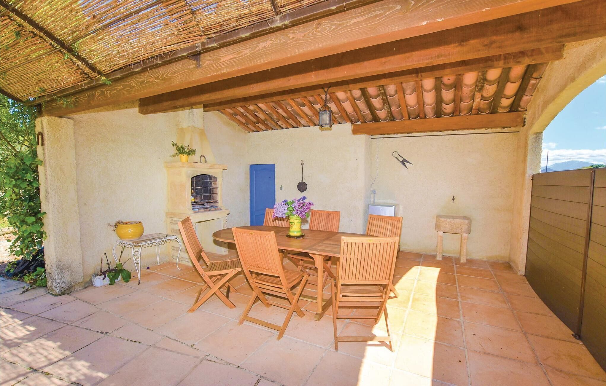Une terrasse extérieure avec une table et des chaises en bois, une petite cheminée et une porte bleue.