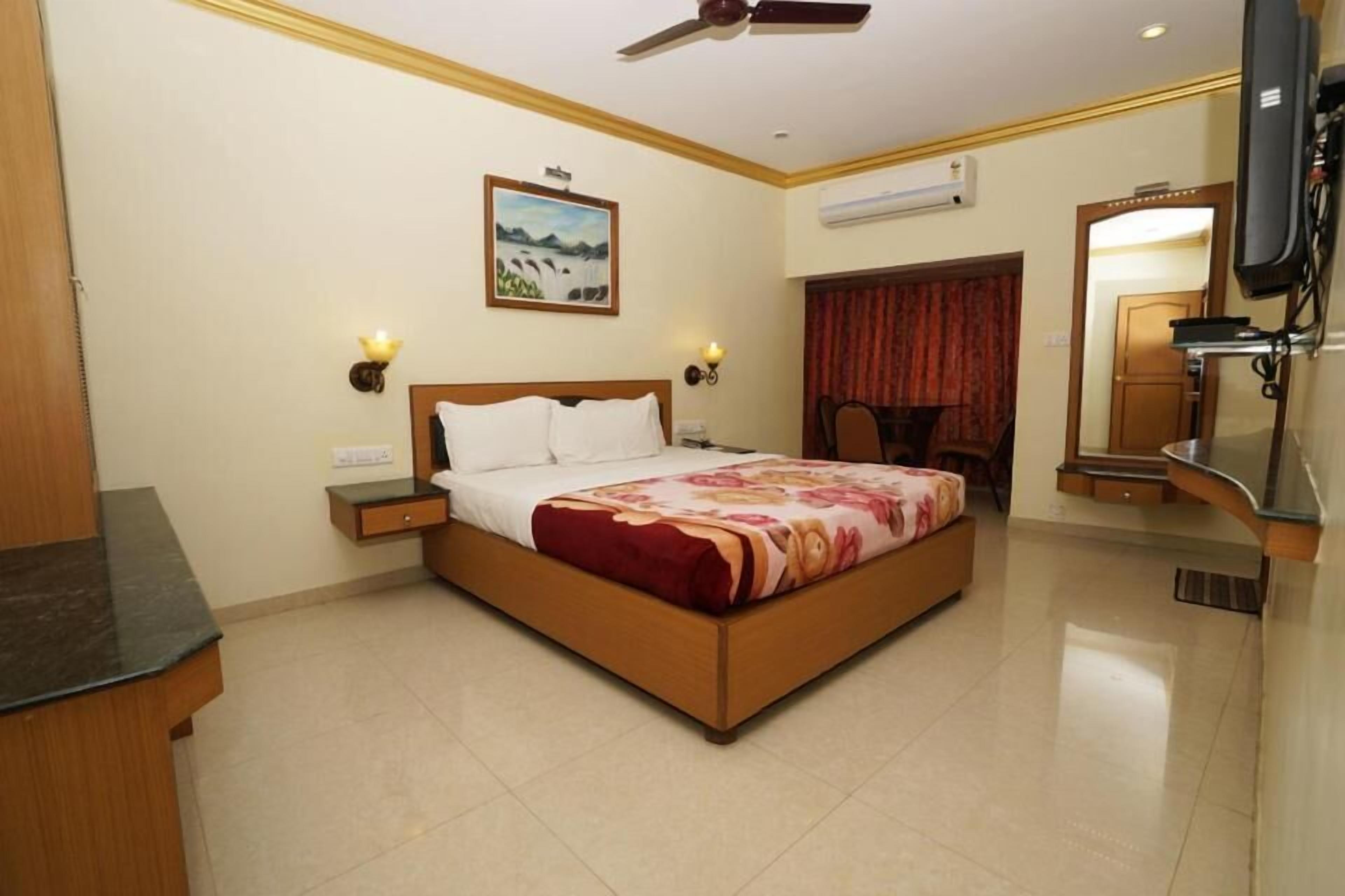 Habitación de hotel con cama, mesitas de noche, ventilador de techo, un cuadro, espejo y unidad de aire acondicionado.