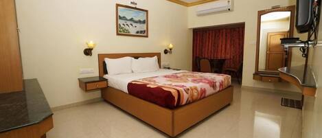 Habitación de hotel con cama, mesitas de noche, ventilador de techo, un cuadro, espejo y unidad de aire acondicionado.