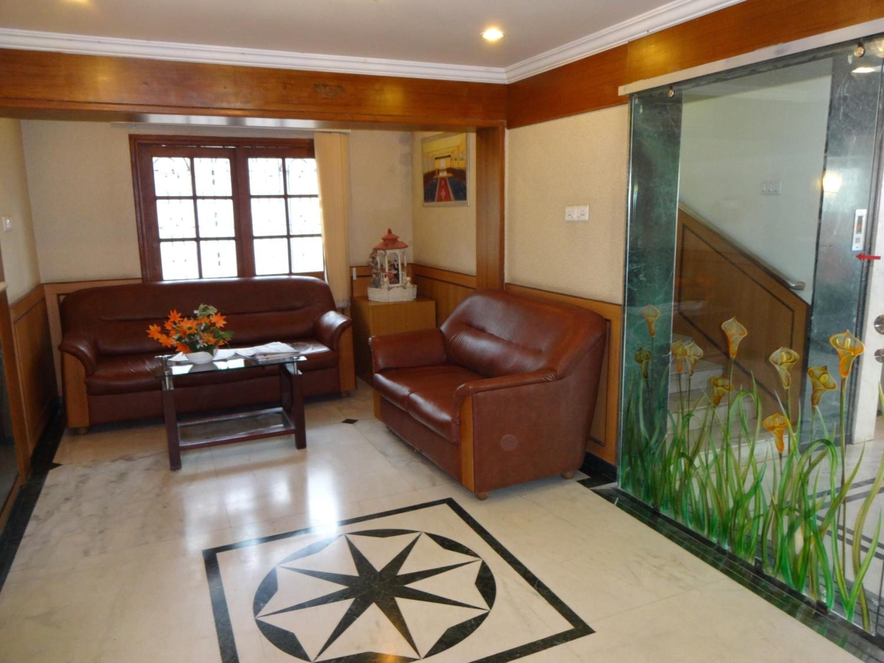 Un vestíbulo con un sofá de cuero marrón, una mesita con un florero y un ascensor de vidrio, además de una pared decorativa con estampado floral.