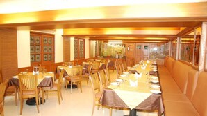 A long dining table with multiple chairs, a sofa, and a decorative wall. - Nahar Manchester Inn (Coimbatore)