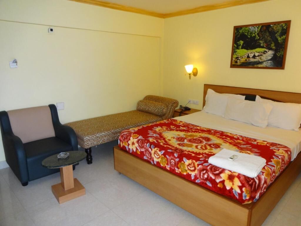 A hotel room with a bed, a chair, a small table, and a painting on the wall.