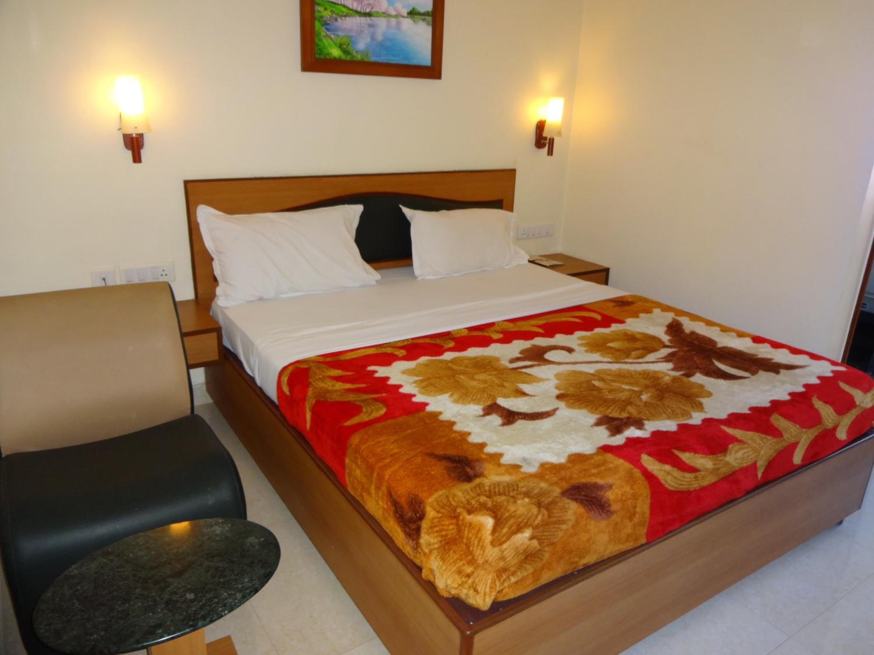 Habitación de hotel con una cama, una silla, una mesita y dos lámparas de pared.