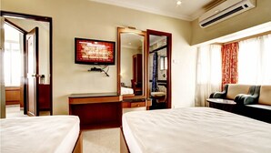 A hotel room with two beds, a desk, a television, a mirror, a sofa, and an air conditioning unit. - Nahar Manchester Inn (Coimbatore)
