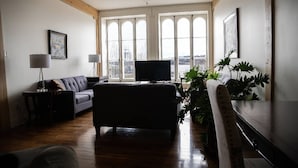 En stue med sofa, fjernsyn og et stort vindue med udsigt over bybilledet.
