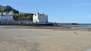 Un hôtel situé sur la côte, avec plusieurs étages, une jetée qui s’avance dans la mer et une plage rocheuse au premier plan.
