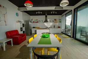 A modern kitchen with a dining area, featuring a red sofa, yellow chairs, and a green bowl on the table.