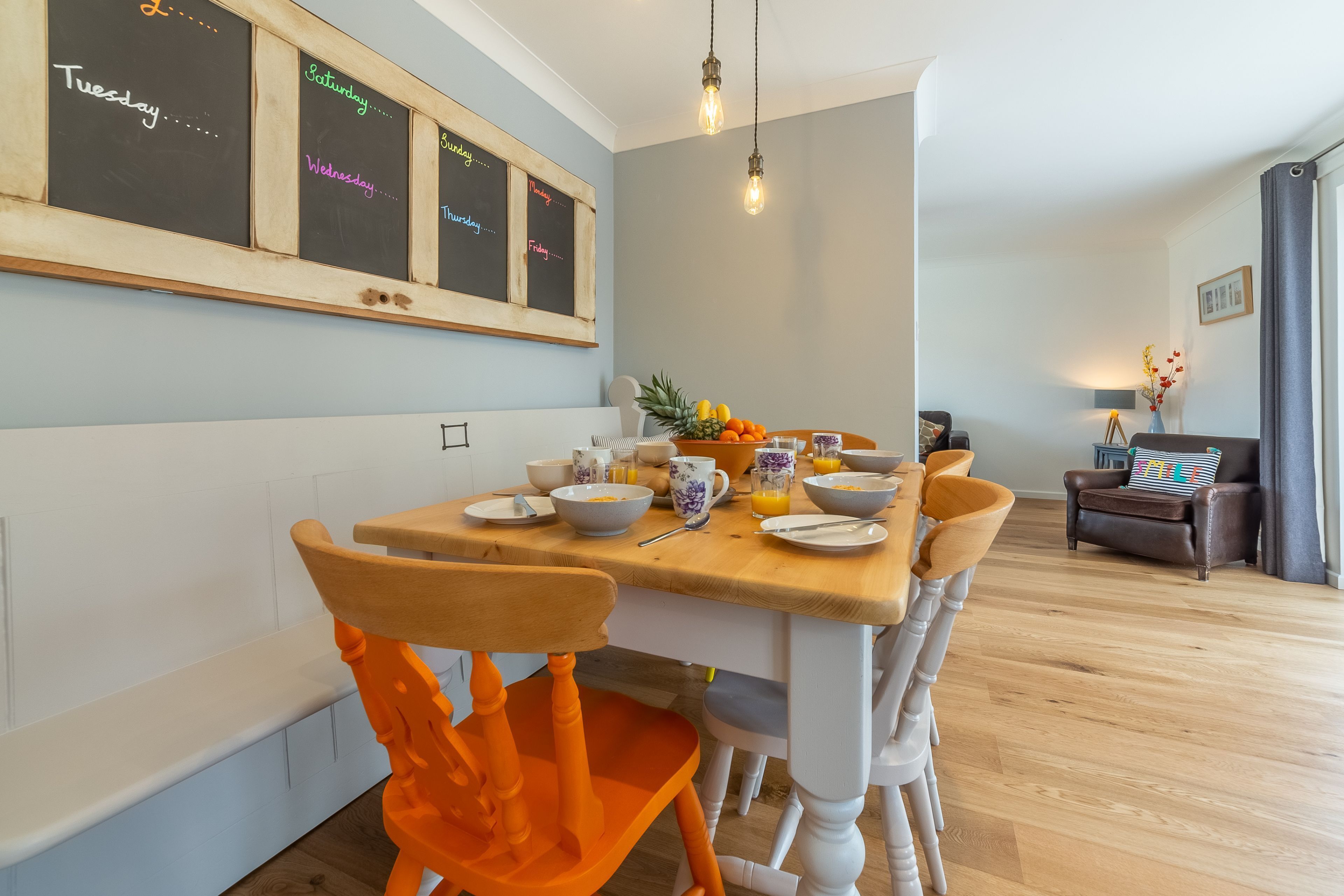 A dining area with a wooden table, chairs, and a chalkboard with days of the week written on it.