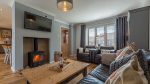 Ein modernes Wohnzimmer mit Kamin, Flachbildfernseher, Sofa und Esstisch.