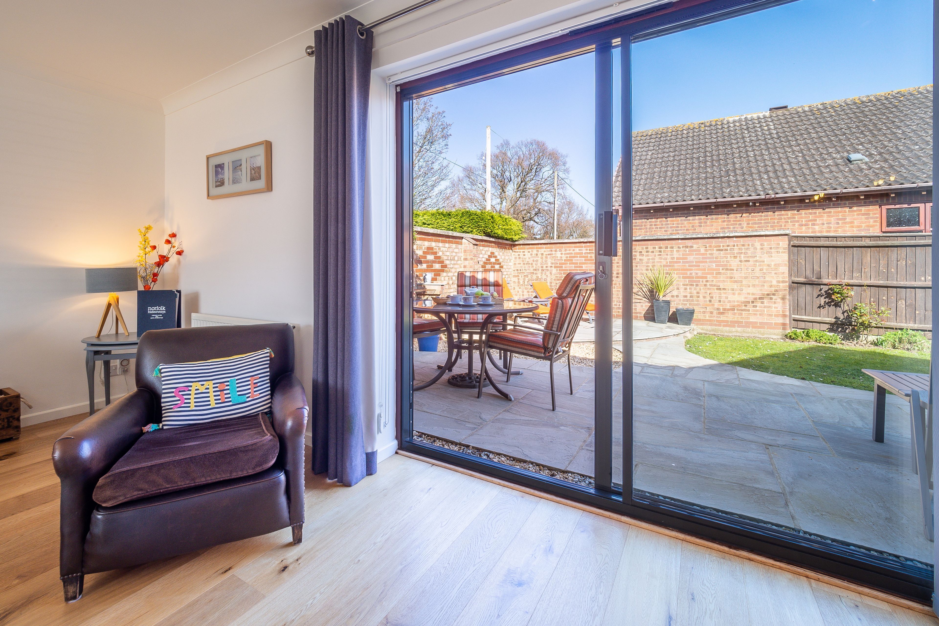 A modern living room with a leather armchair, a glass door leading to a patio with outdoor furniture.