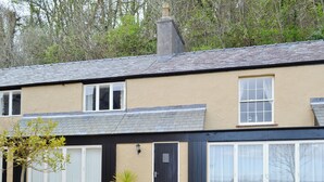 A two-story house with a grey tiled roof, beige walls, and a small garden area with gravel and a potted plant. - 1 bedroom accommodation in Llandudno (Llandudno)