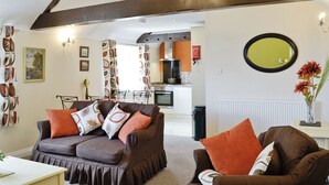 A living room with a brown sofa, a dining table, and a kitchen in the background. - 1 bedroom accommodation in Llandudno (Llandudno)