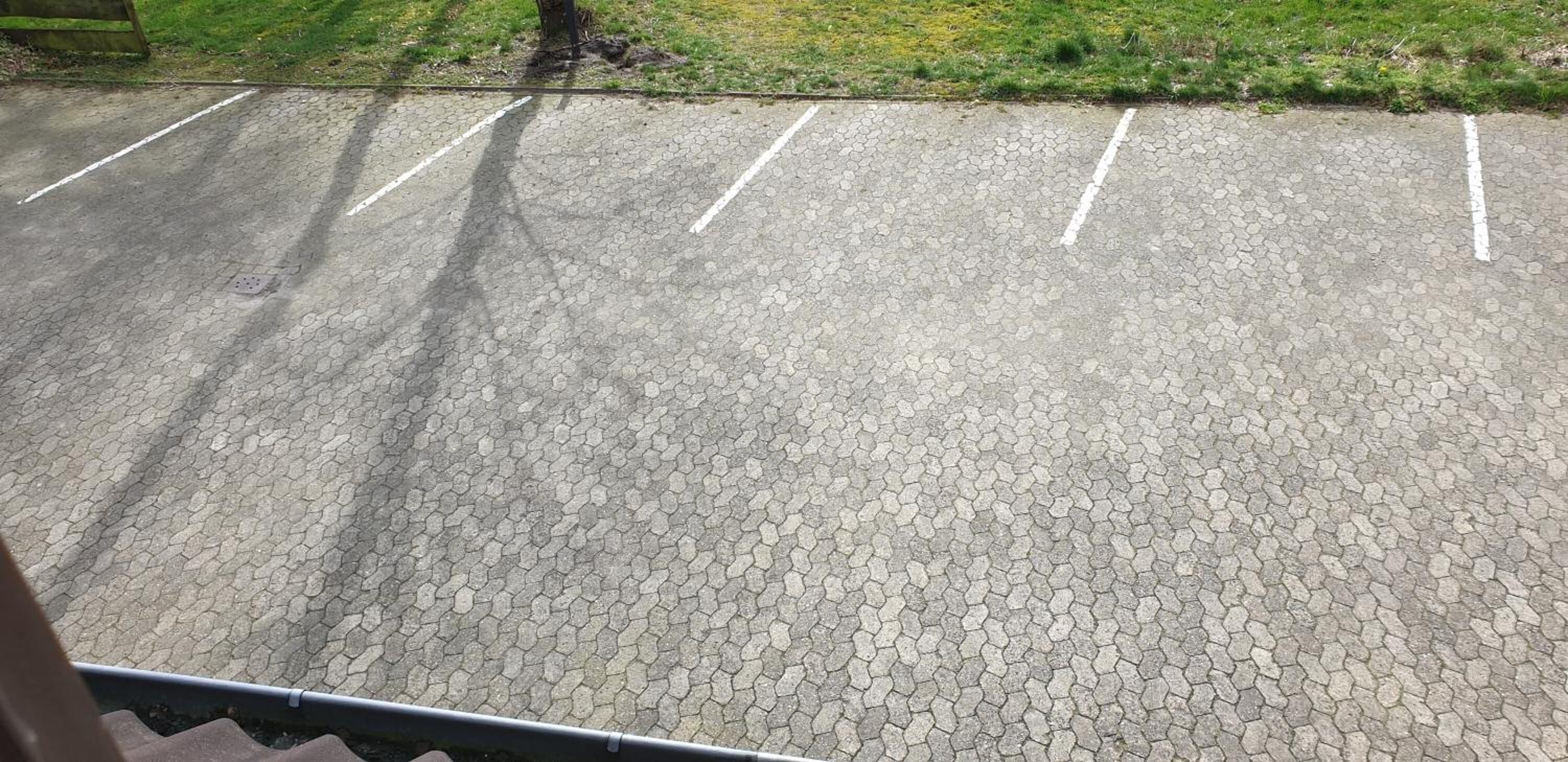 En parkeringsplads med sekskantet belægning og hvide linjer, der afgrænser parkeringsbåsene.