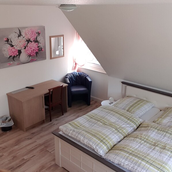 A bedroom with a bed, a desk, a chair, a trash bin, and a painting on the wall. - Gästehaus Strudthoff (Ganderkesee)