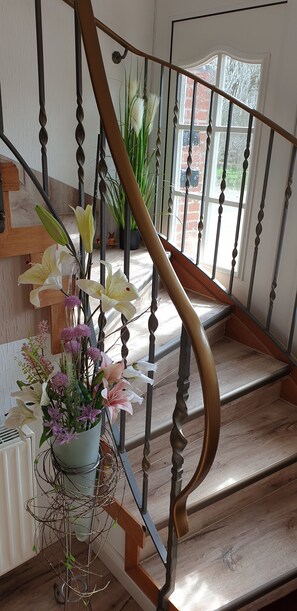 A wooden staircase with a metal railing, a potted plant with flowers, and a brick wall in the background. - Gästehaus Strudthoff (Ganderkesee)