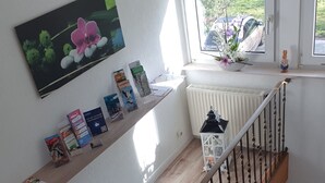 Uma escada com corrimão de madeira, um radiador branco e uma prateleira com livros e um vaso pequeno.