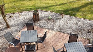 Um pátio externo com piso de tijolos, ladeado por brita e gramado.