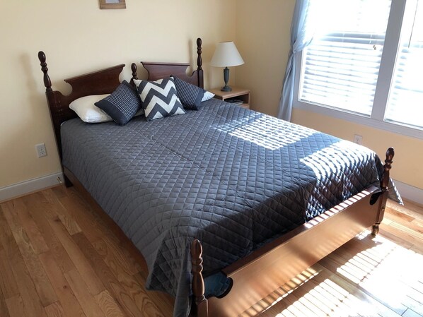Een slaapkamer met een houten bed, een nachtkastje met een lamp en een raam met blinds.