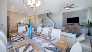 Un espace repas moderne avec une table en bois dressée pour six personnes, des chaises blanches et un lustre.