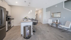 Une cuisine moderne dotée d’appareils électroménagers en acier inoxydable, d’un îlot central et d’un coin repas avec une chaise et une table blanches.