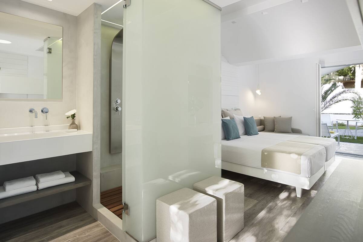 Une chambre d’hôtel moderne dotée d’une douche à parois de verre, d’un grand lit avec des oreillers, d’une table de chevet et offrant une vue sur l’extérieur.