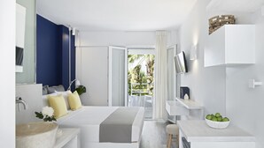 Una habitación de hotel moderna con una cama, un baño con lavabo y espejo, un escritorio pequeño con un frutero, y vistas al exterior.