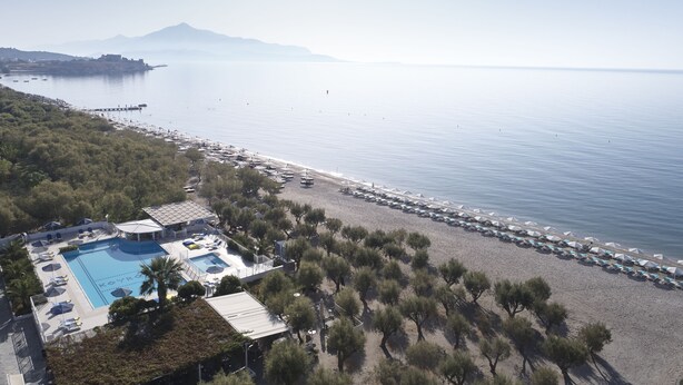 Vista aérea de un complejo turístico costero con piscina, sombrillas de playa y un muelle.