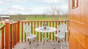 A wooden deck with two ornate white chairs and a small round table, overlooking a green landscape. - 1 bedroom accommodation in Near The New Forest (Near The New Forest)