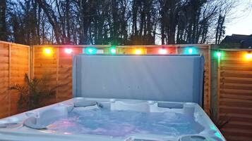Un bain à remous doté d’un panneau de commande, entouré d’une clôture en bois et illuminé de guirlandes lumineuses.