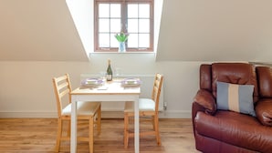 A dining area with a white table set for four, a brown leather sofa, and a window with a view. - 1 bedroom accommodation in Near The New Forest (Near The New Forest)