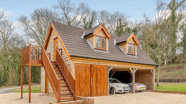 A wooden cabin with a garage, a staircase, and two cars parked inside. - 1 bedroom accommodation in Near The New Forest (Near The New Forest)