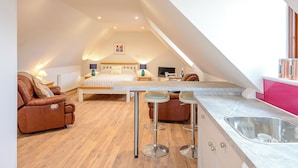 A modern loft bedroom with a large bed, a sitting area, and a kitchenette. - 1 bedroom accommodation in Near The New Forest (Near The New Forest)