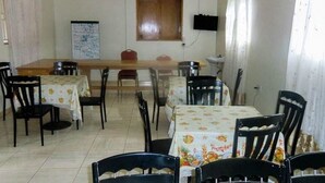 A dining area with multiple tables and chairs, a wooden cabinet, a whiteboard, and a television on the wall. - Palm Springs Hotel (Masaka)