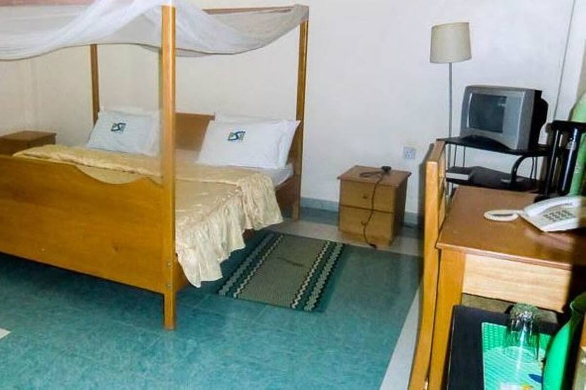 A room with a four-poster bed, a desk with a telephone, a small cabinet, and a television.