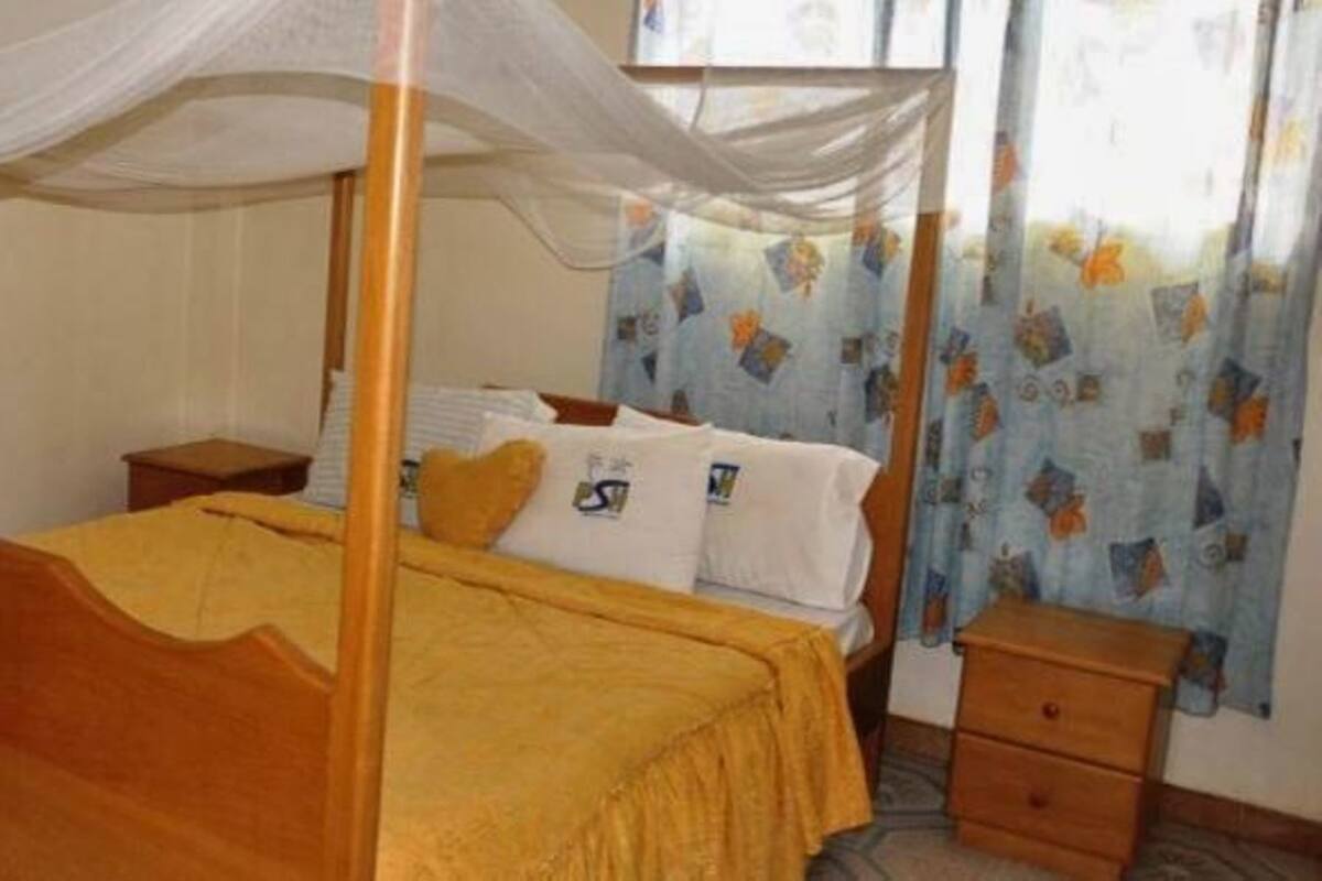 A four-poster bed with a yellow bedspread, a wooden nightstand, and a small drawer unit.