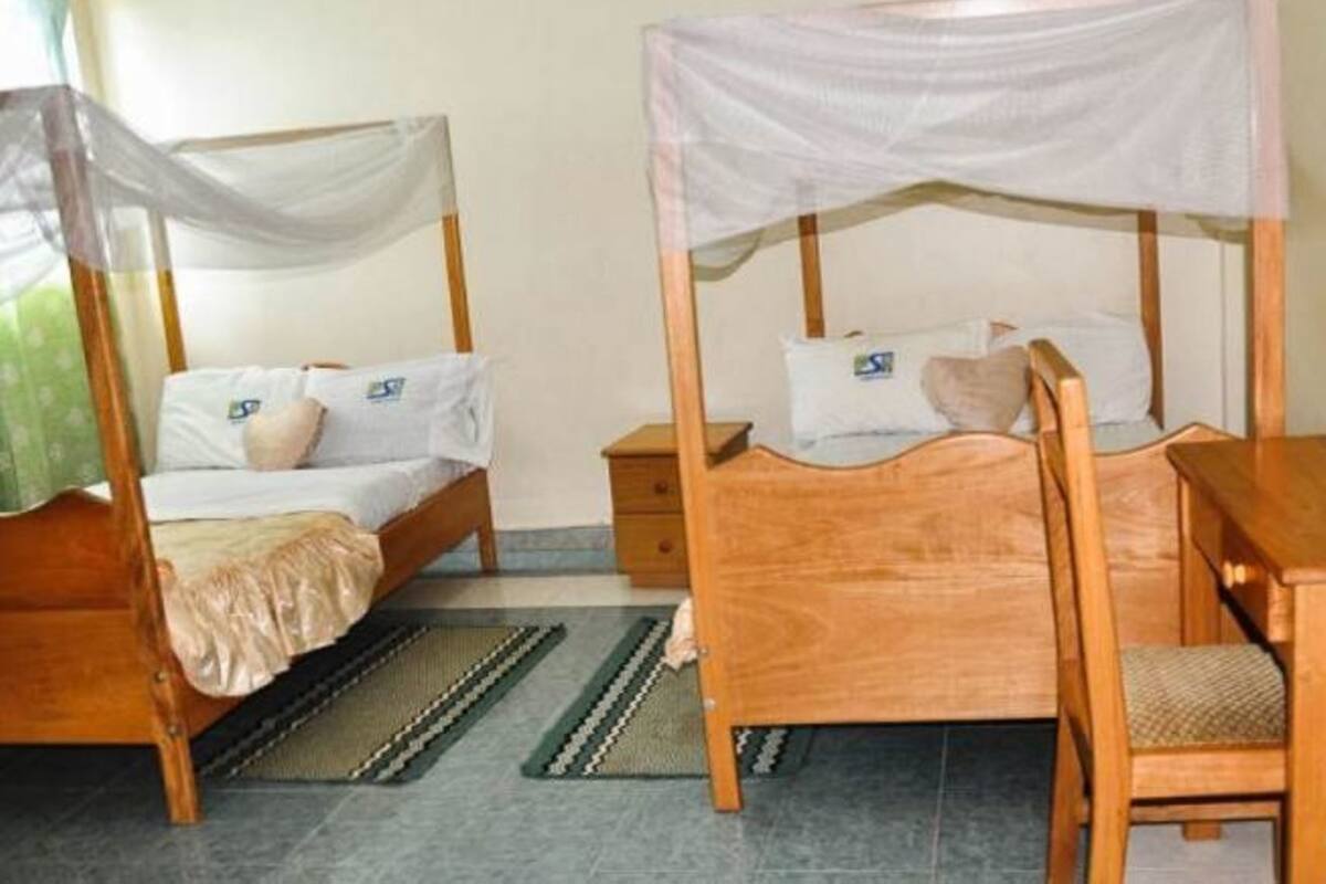A room with two wooden beds, each with a canopy, a small wooden nightstand, a chair, and a table.