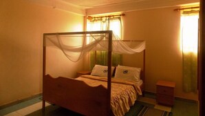 A four-poster bed with a canopy, a bedside table, and a nightstand. - Palm Springs Hotel (Masaka)