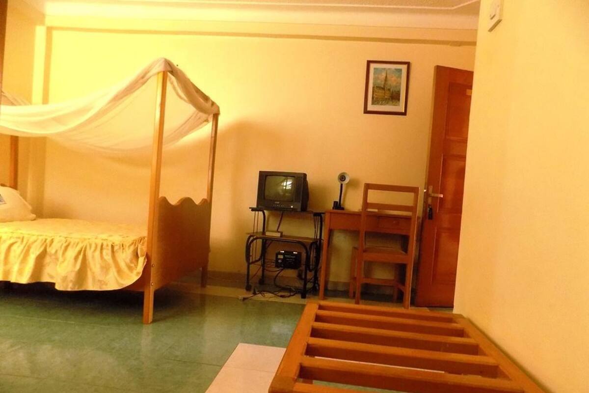 A room with a bed, a television, a chair, and a wooden bench.