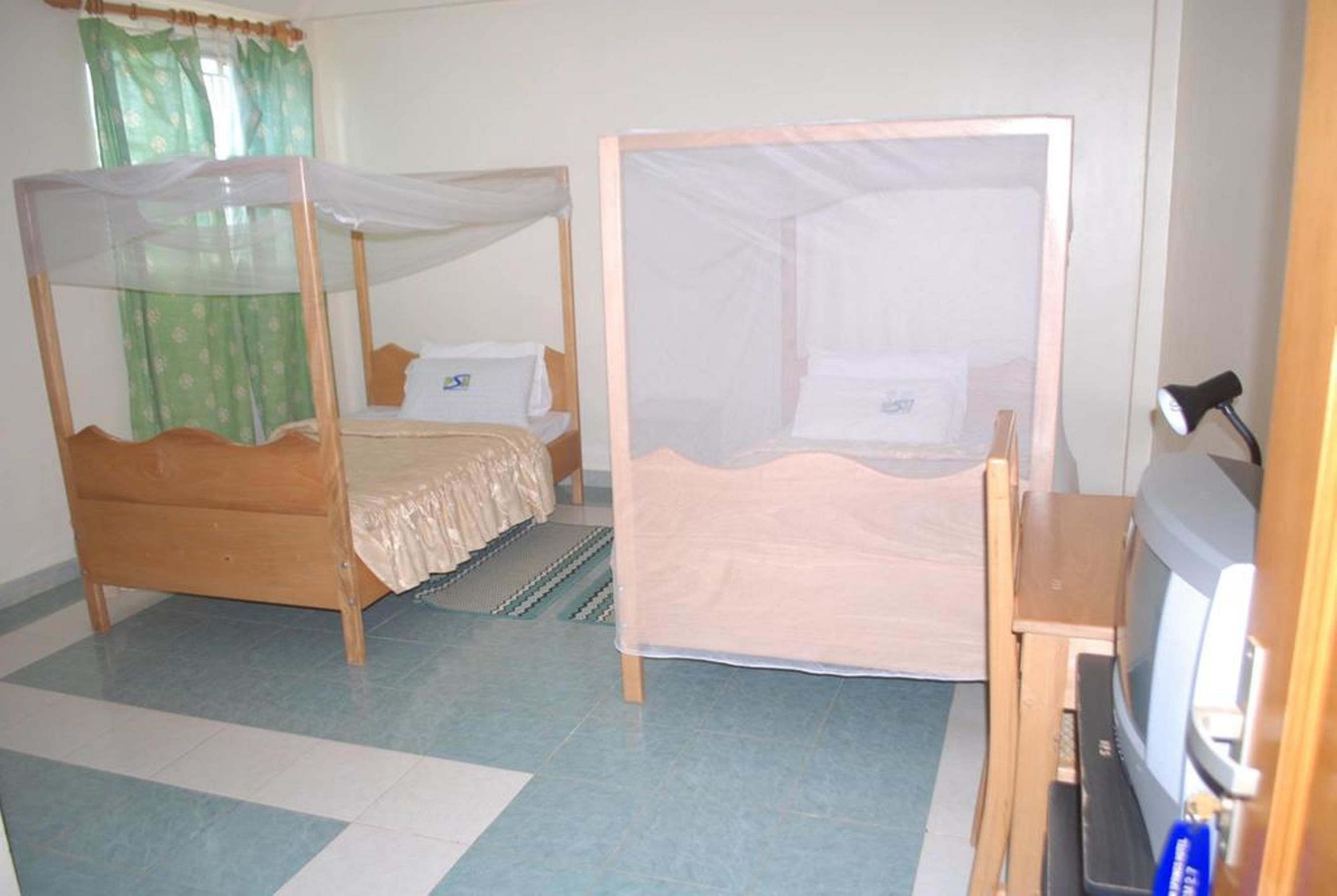 A room with two wooden beds with white canopies, a small television on a wooden stand, and a green curtain.
