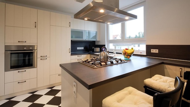 Una cocina moderna con armarios blancos, una isla central con asientos, una estufa y un amplio ventanal que proporciona luz natural.