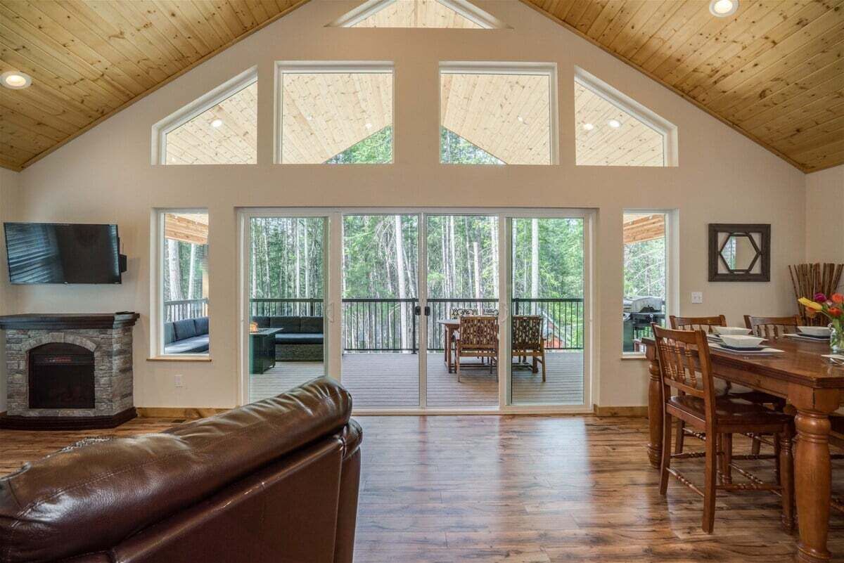 A spacious room with a stone fireplace, a leather couch, a dining table with chairs, and large windows offering a view of the outdoors.