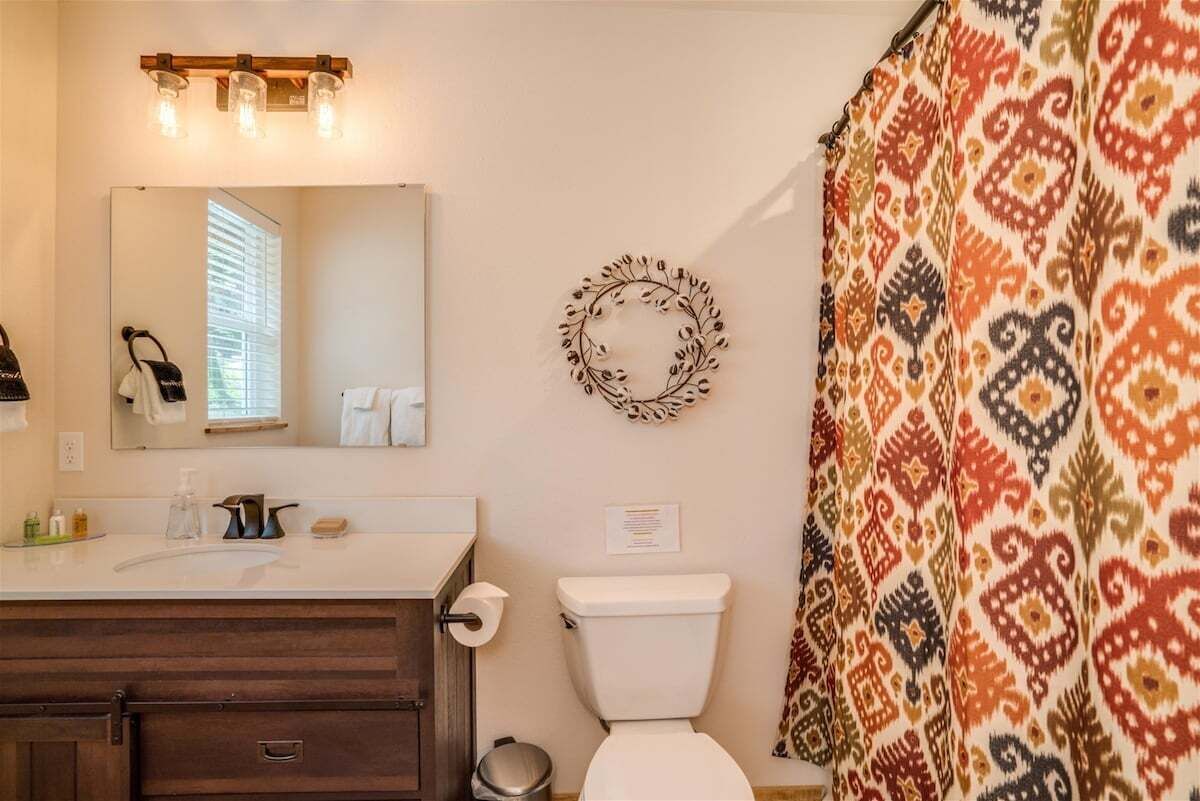 A bathroom with a white toilet, a mirror, a sink with a soap dispenser, and a shower curtain with a patterned design.