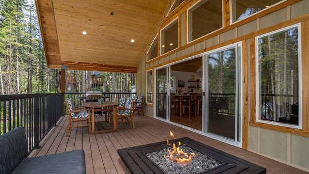 A covered deck with a fire pit, outdoor furniture, and large windows.