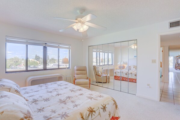 A bedroom with a bed, a chair, a ceiling fan, and a large window.