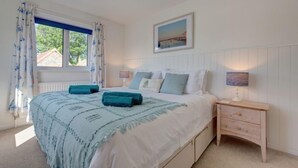 A bedroom with a bed, a nightstand, a window with curtains, and a wall-mounted picture. - Egret, South Creake, Norfolk (South Creake)